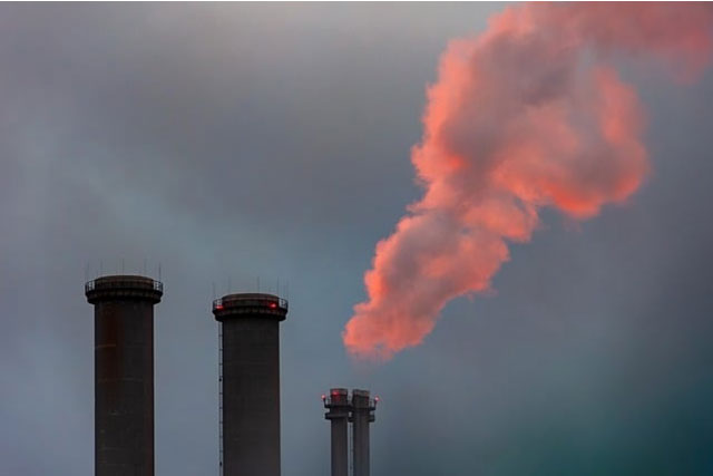 Industrial chimneys releasing emissions against a sunset sky, symbolizing China’s climate adaptation and energy transition challenges.